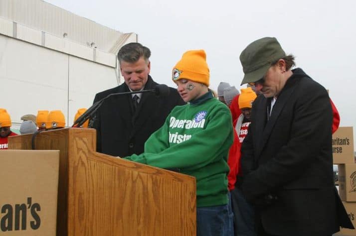 Lesley Clementi flanked by Franklin Graham (left) and musician Bono (right) pray during a special send-off for Operation Christmas Child shoebox gifts being airlifted to Uganda.