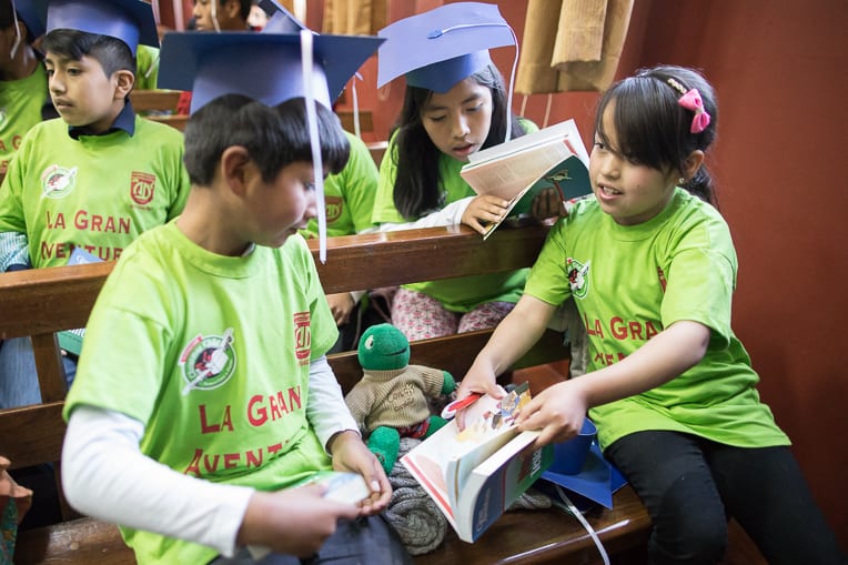 Daphne, right, shows her The Greatest Journey classmate the colorful illustrations included in the New Testaments they each received as part of their graduation ceremony.