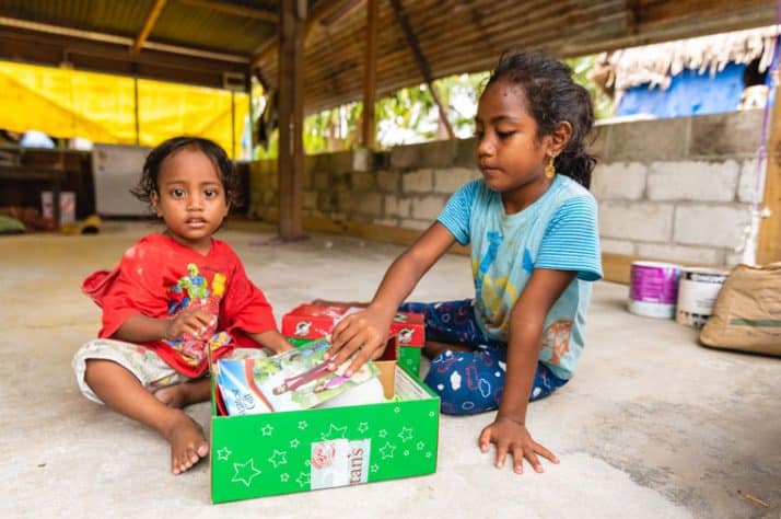 A girl shows her sister the shoebox gift she received during the outreach event in her village.