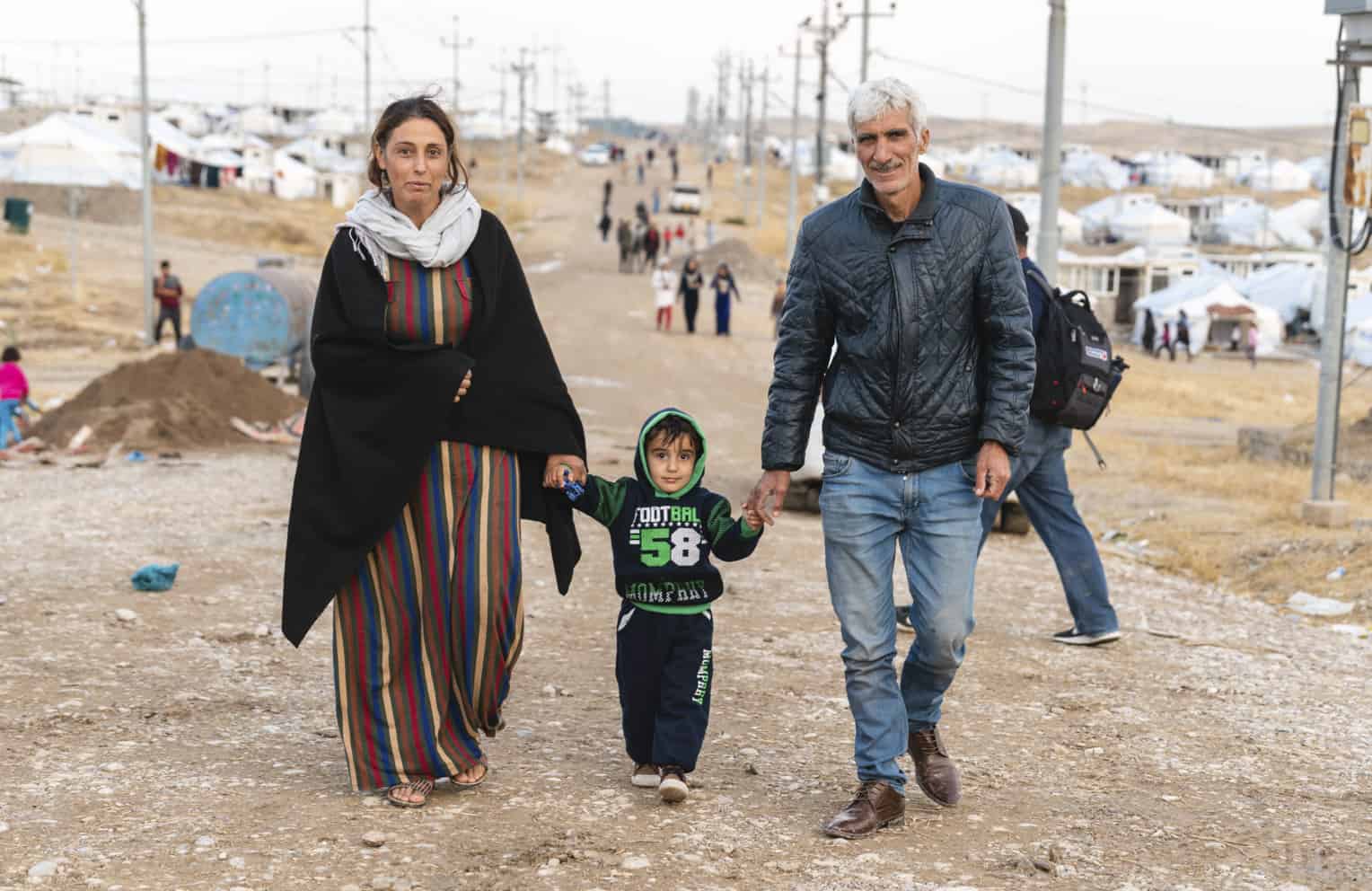 Mirko and his wife and young son walk down the road in Bardarash camp.