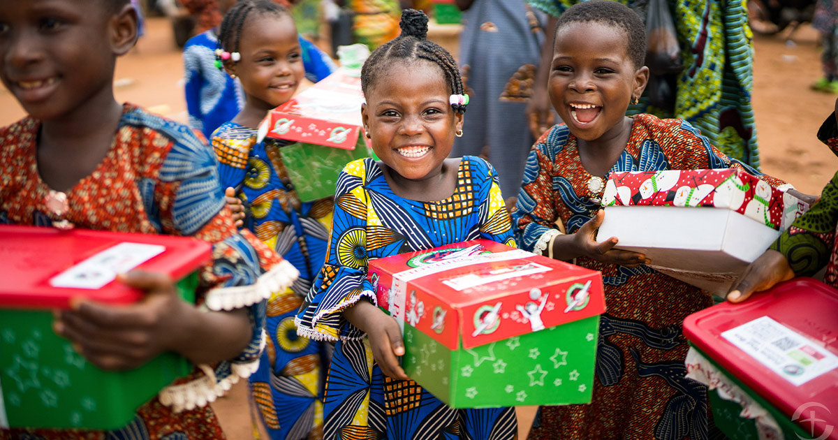 A child smiles as they hold an Operation Christmas Child shoebox gift, a reminder that God uses simple gifts to share the Good News of Jesus.