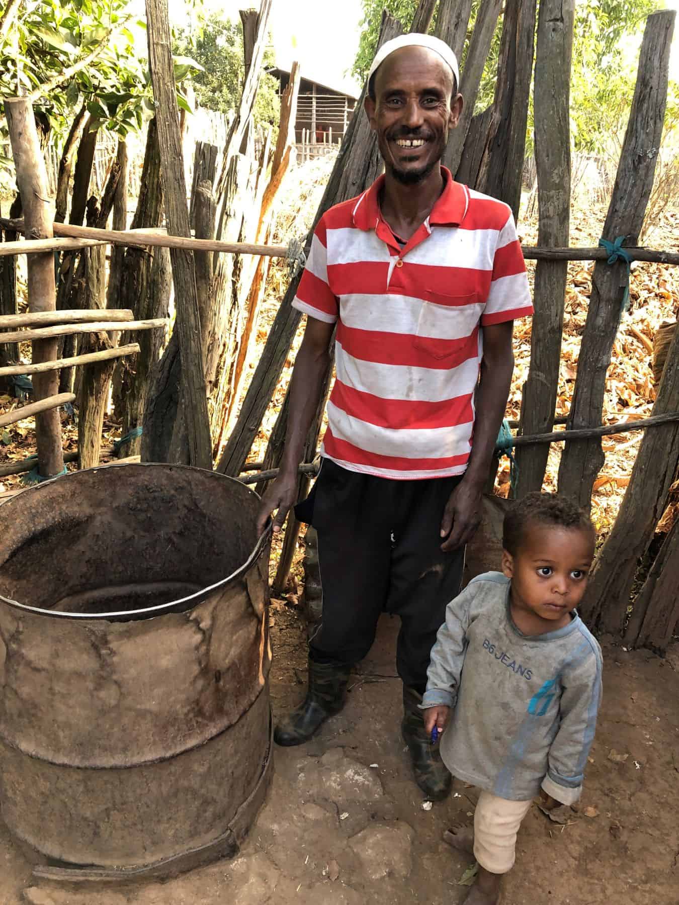 Dinake Hussan smiles while standing with his son beside their family well, knowing their BioSand Filter is making the well water safe to drink