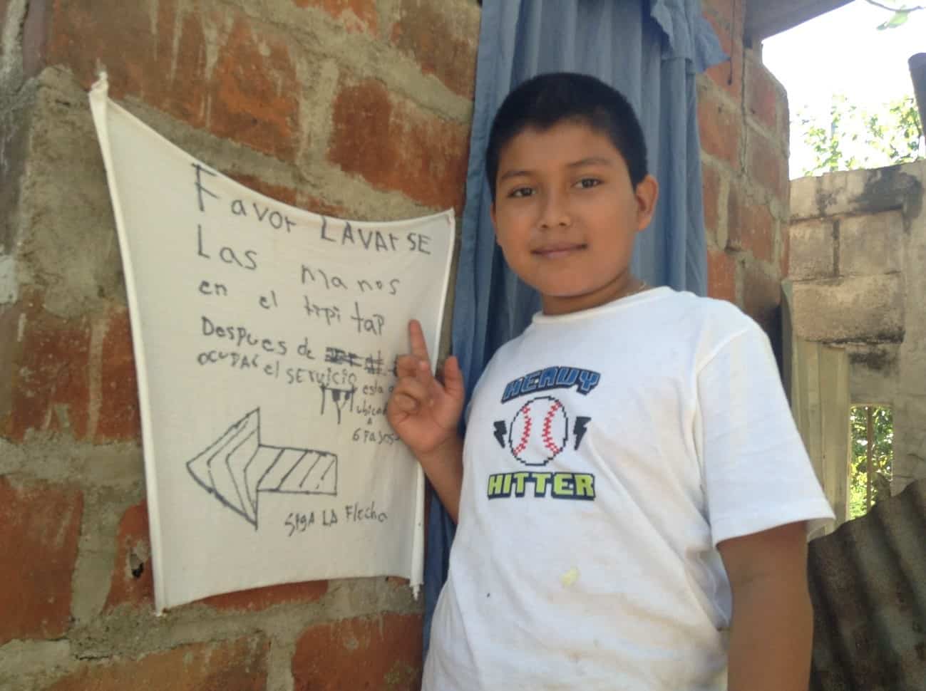 Julio alongside a sign pointing the way to his family’s tippy-tap handwashing station.