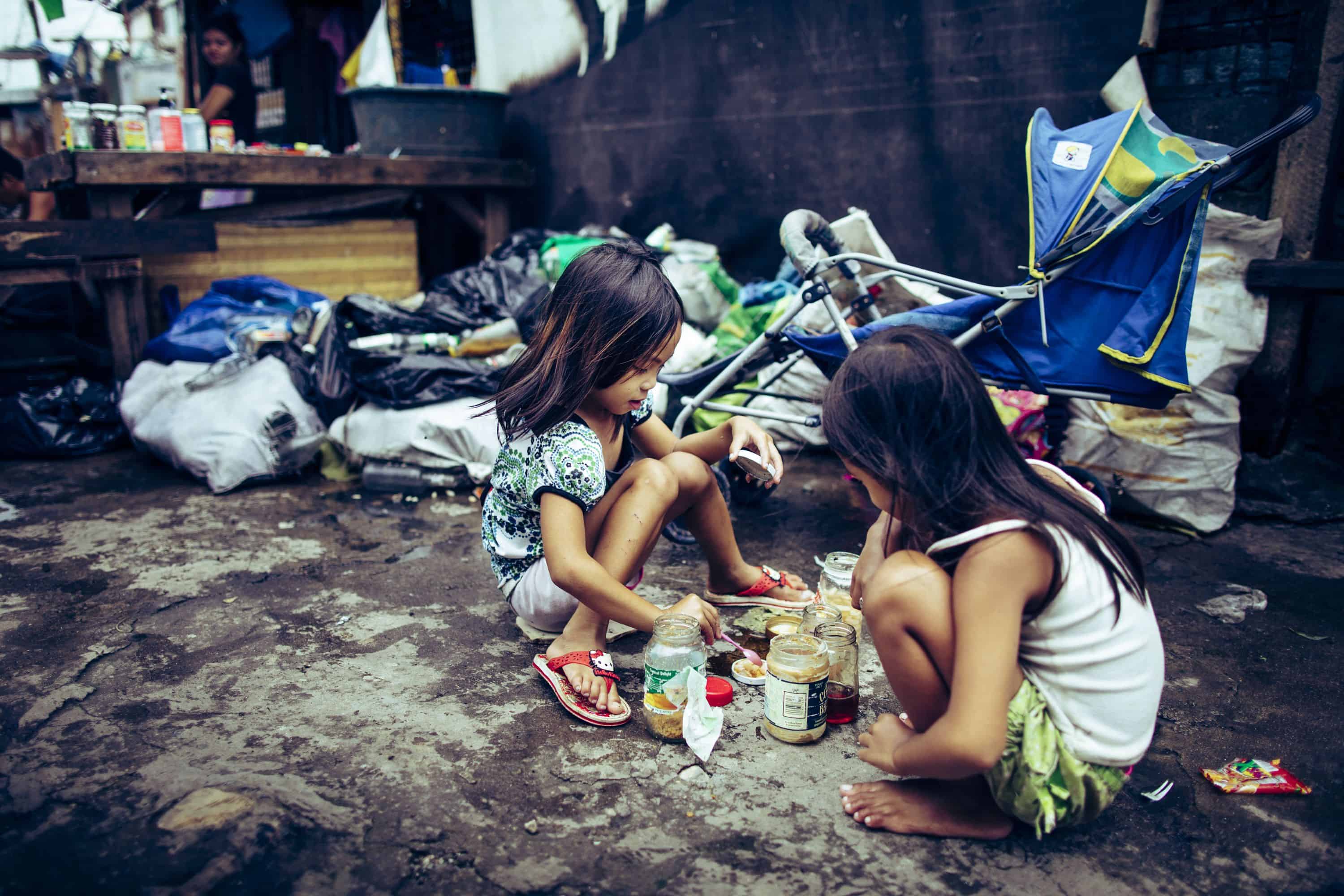 Children make the best of what they have, as these girls enjoy a pretend game of “house” and prepare food in their kitchen.