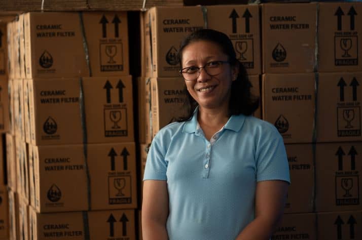 Janella stands in front of components for water filters that she is using to reach her neighbors with life-giving safe water.
