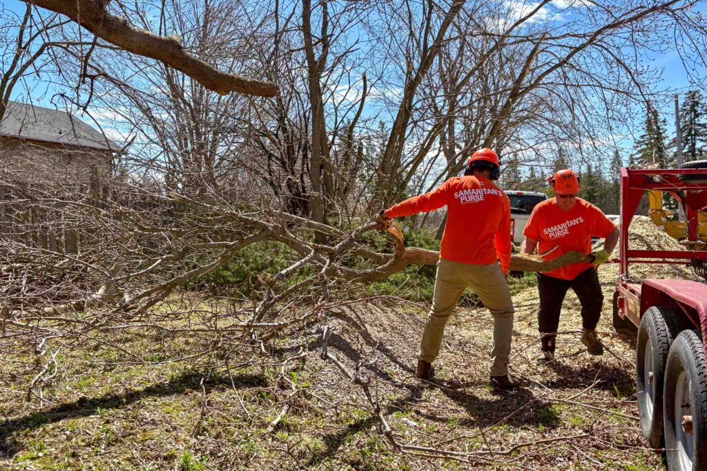 Two volunteers clearing away branches from a home.