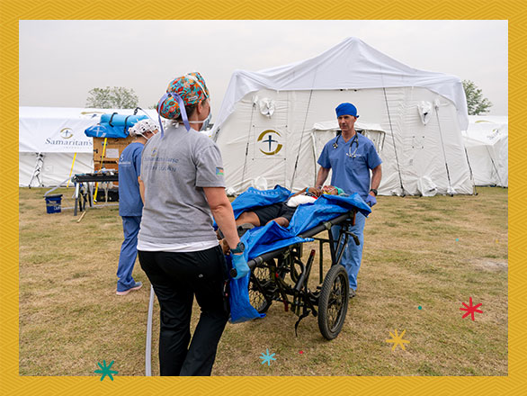 An overview of a busy Samaritan's Purse Emergency Field Hospital shows doctors and nurses treating multiple patients in a large medical tent, the same environment where Sanda's life-saving surgery was performed.