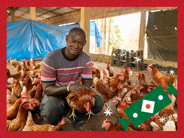 Pastor Ernest kneels inside his chicken coop, holding one of the many healthy chickens he now raises to provide food for his family and community, and income through selling eggs.
