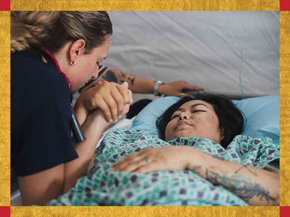 A compassionate Samaritan's Purse nurse holds the hand of a patient, representing the critical and heartfelt medical care Sanda received after being rescued from a collapsed building following an earthquake.
