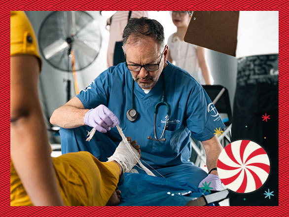 A doctor carefully treats a patient's bandaged leg, illustrating the urgent surgical care Sanda needed for her deeply wounded leg after being trapped in rubble for hours.
