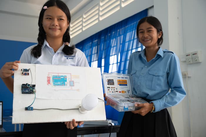 Lysa and a classmate stand together, proudly presenting a completed electronics project they built, showcasing their newfound skills and the confidence they've gained through the STEM program.