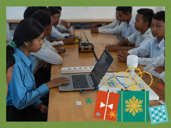 Lysa and her classmates collaborate around a table, using a laptop and a circuit board to work on a hands-on science project, demonstrating the engaging learning that helps them overcome educational barriers.