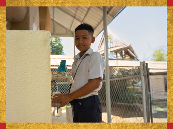 A smiling Kakada fills his water bottle from a new community BioSand Filter at his school, a symbol of the life-changing gift of safe, clean drinking water.
