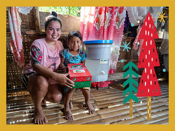 A smiling mother and her young child proudly display their new household water filter, showing how the gift of safe water brings health and joy directly into the home.