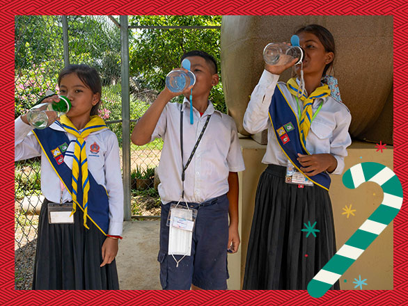 akada and his schoolmates in their scout uniforms confidently drink clean water from their personal bottles, now free from the fear of waterborne diseases like typhoid that once plagued them.
